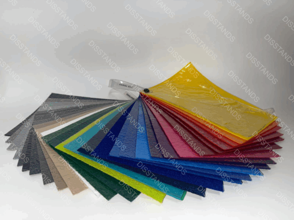 Muestrario profesional en formato abanico mostrando la gama completa de colores de moqueta ferial ecológica disponible en Disstands Barcelona. La imagen muestra más de 20 opciones cromáticas incluyendo tonos neutros (negro, gris, beige), colores corporativos (azul, verde, rojo) y tonos vibrantes (amarillo, naranja) para eventos y ferias. Todas las muestras corresponden a moqueta certificada ignífuga M1, fabricada con materiales reciclables y disponible en stock permanente para instalación profesional en 24-48 horas. Ideal para stands, eventos corporativos, ferias y exposiciones que requieren certificación medioambiental.