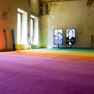 Instalación artística de moqueta multicolor con degradado arcoíris en espacio industrial, colores rosa, naranja, amarillo, verde y azul